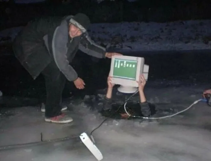Person holding old computer monitor above icy water with another person nearby