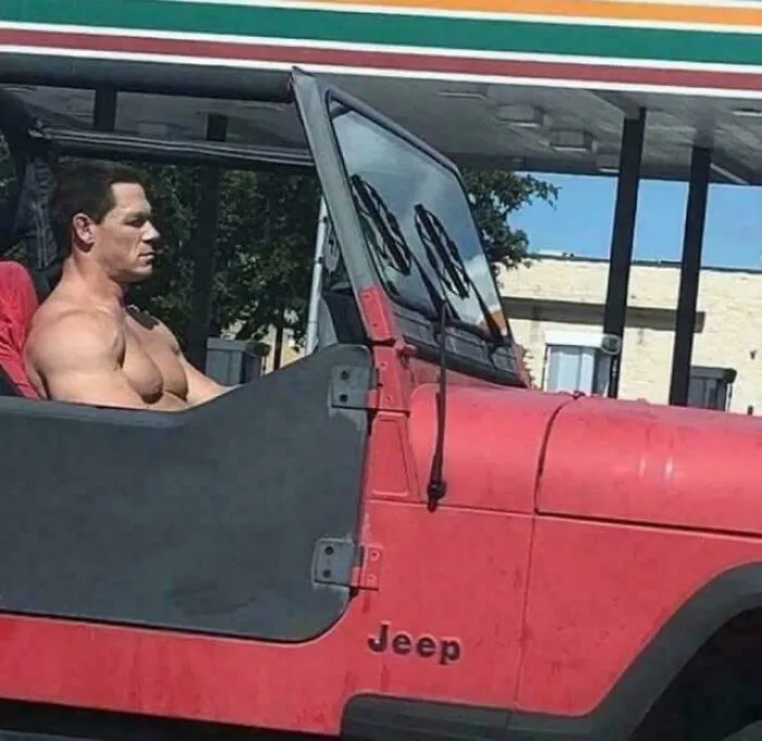 Muscular man sitting shirtless in a red Jeep at gas station