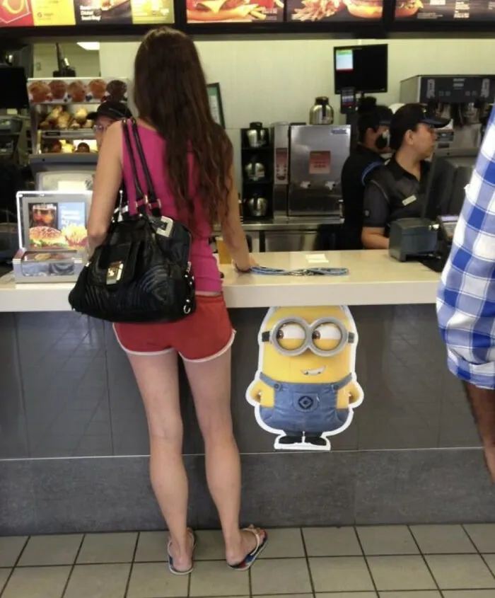 Woman standing at counter with Minion cutout creating a funny illusion