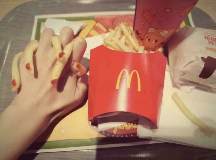 Hand intertwined with fries that have ketchup resembling fingernails