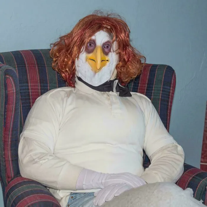 Person in bird costume sitting in armchair wearing red wig