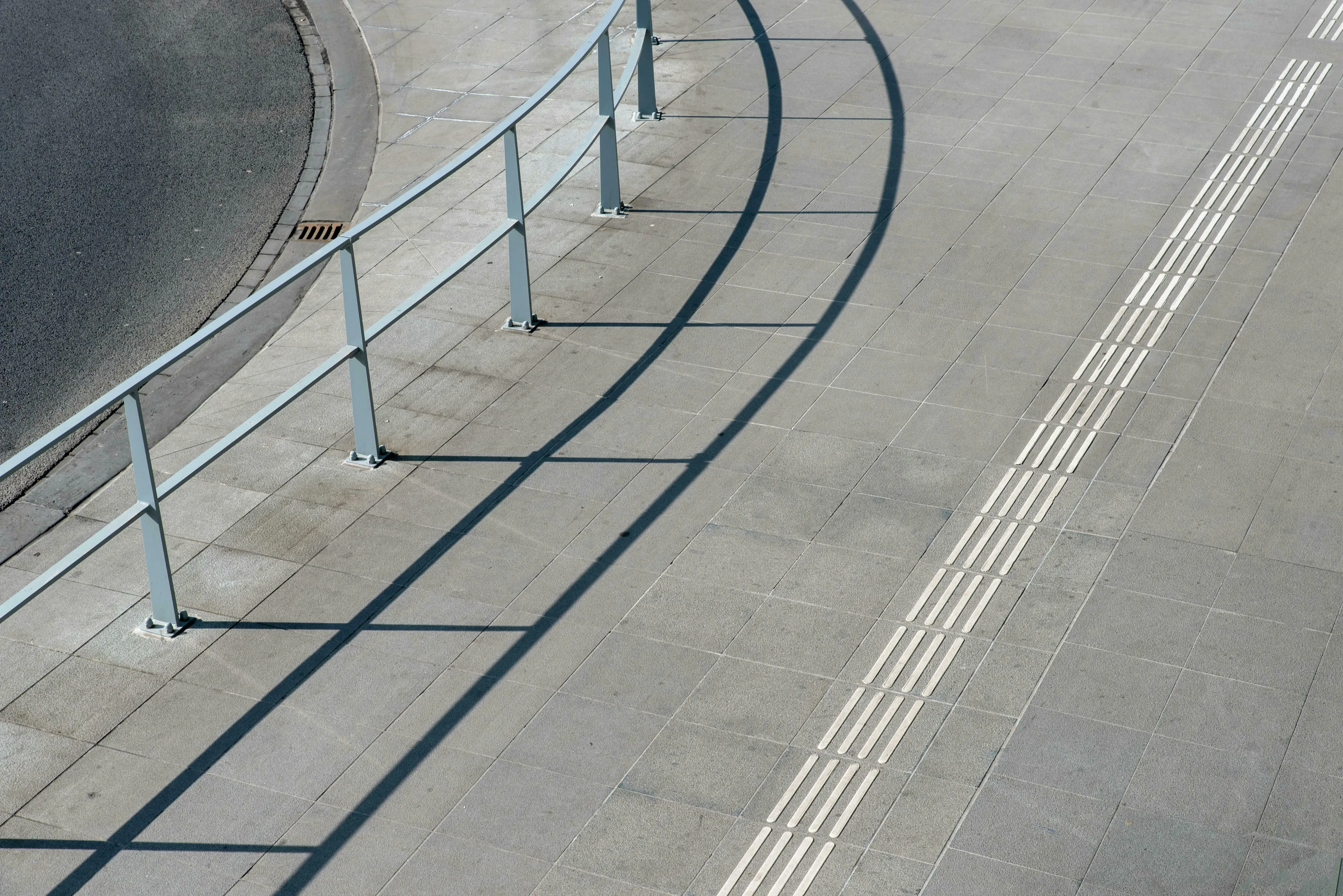 A tiled path with a metal railing casting shadows, next to a road, illustrating American vs British English words.
