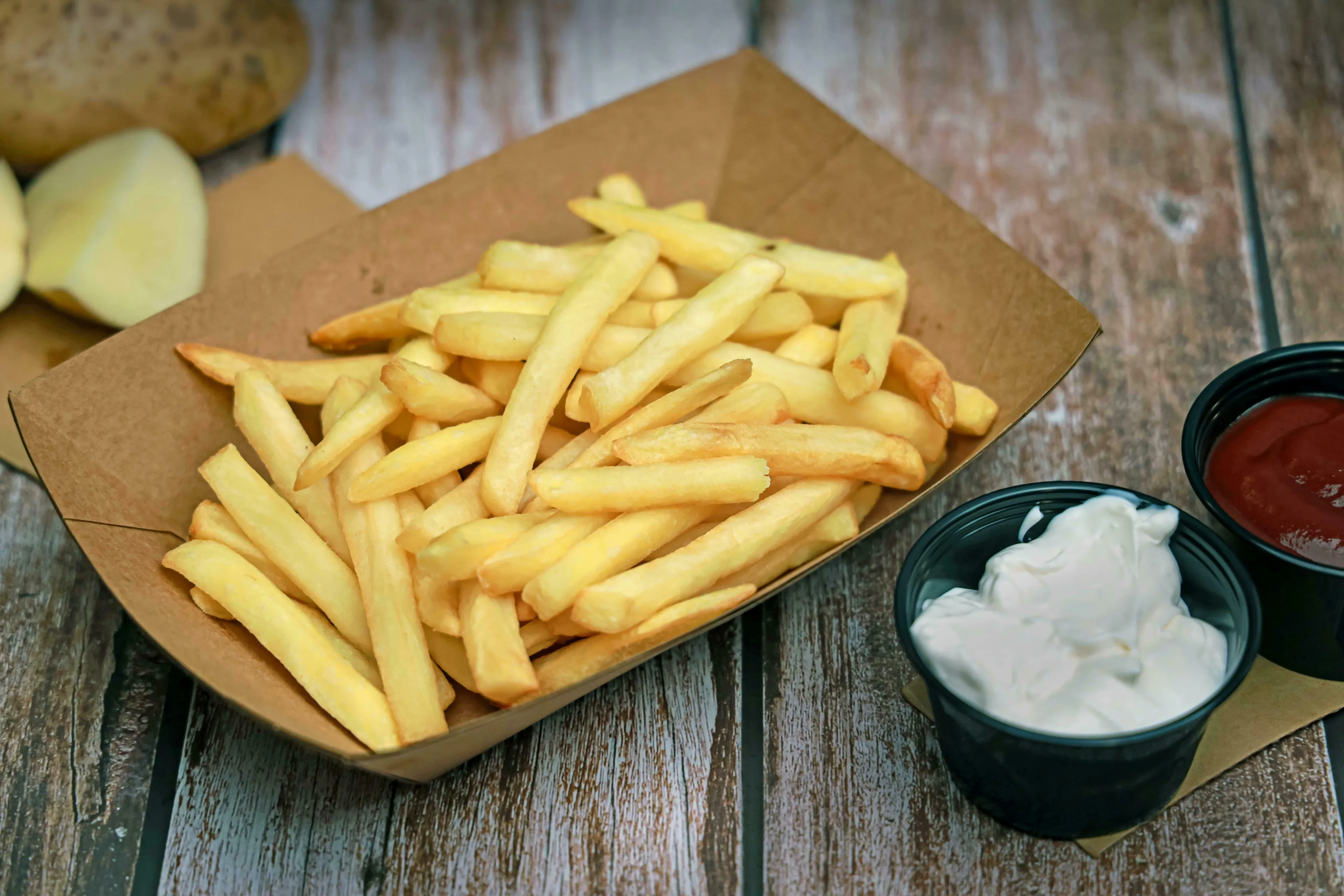 Golden french fries in a paper tray, with small bowls of ketchup and mayonnaise, for an American vs British English words quiz.