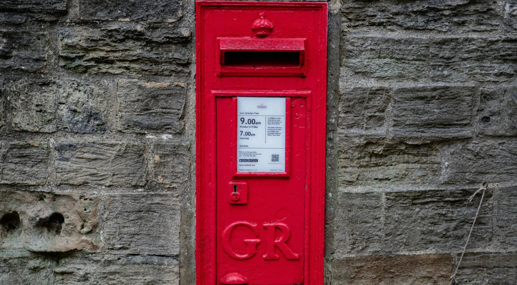 A classic British red post box, or pillar box, set into a stone wall. American vs British English words quiz.