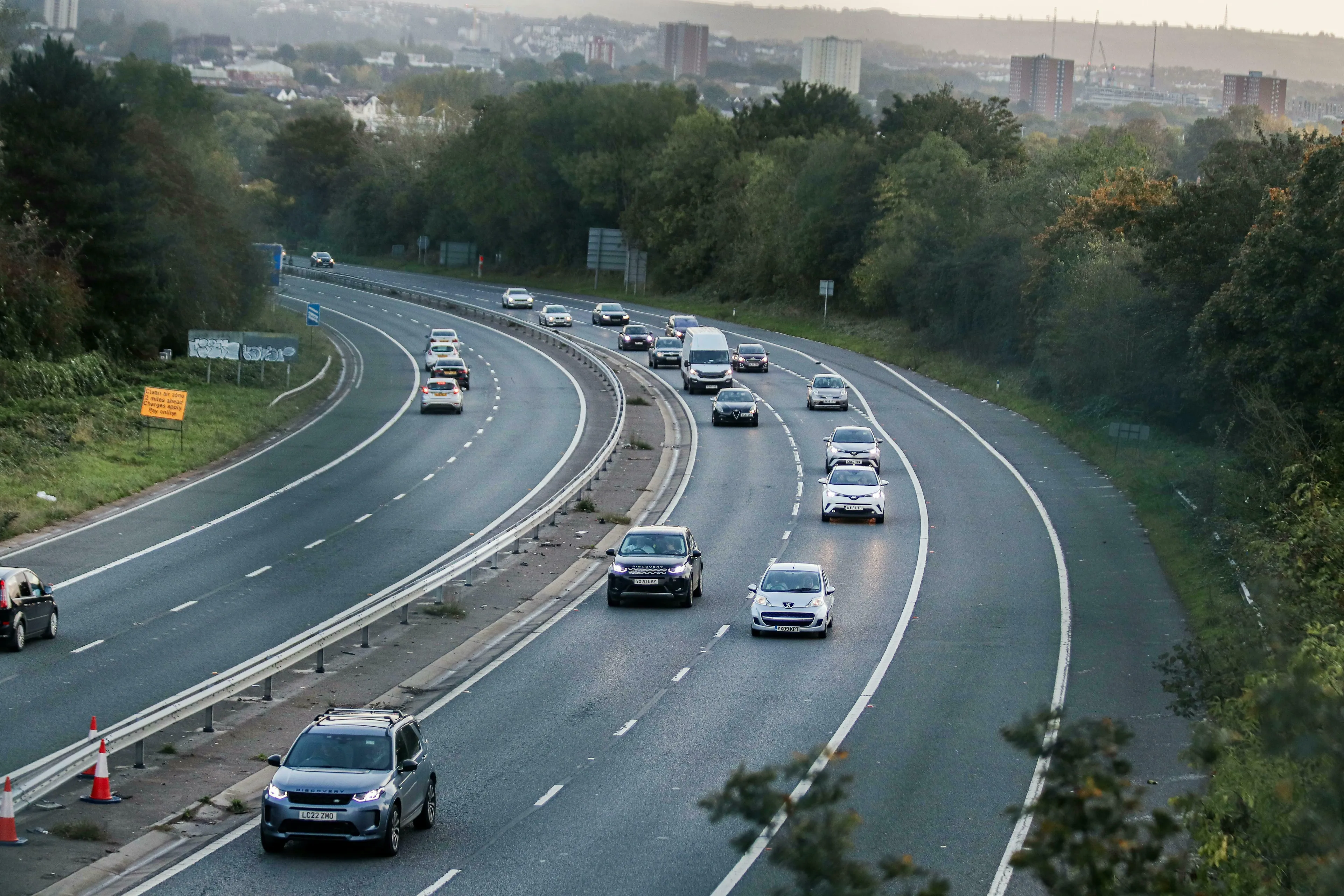 British English quiz: A busy multi-lane motorway curves with traffic, trees, and buildings in the background.