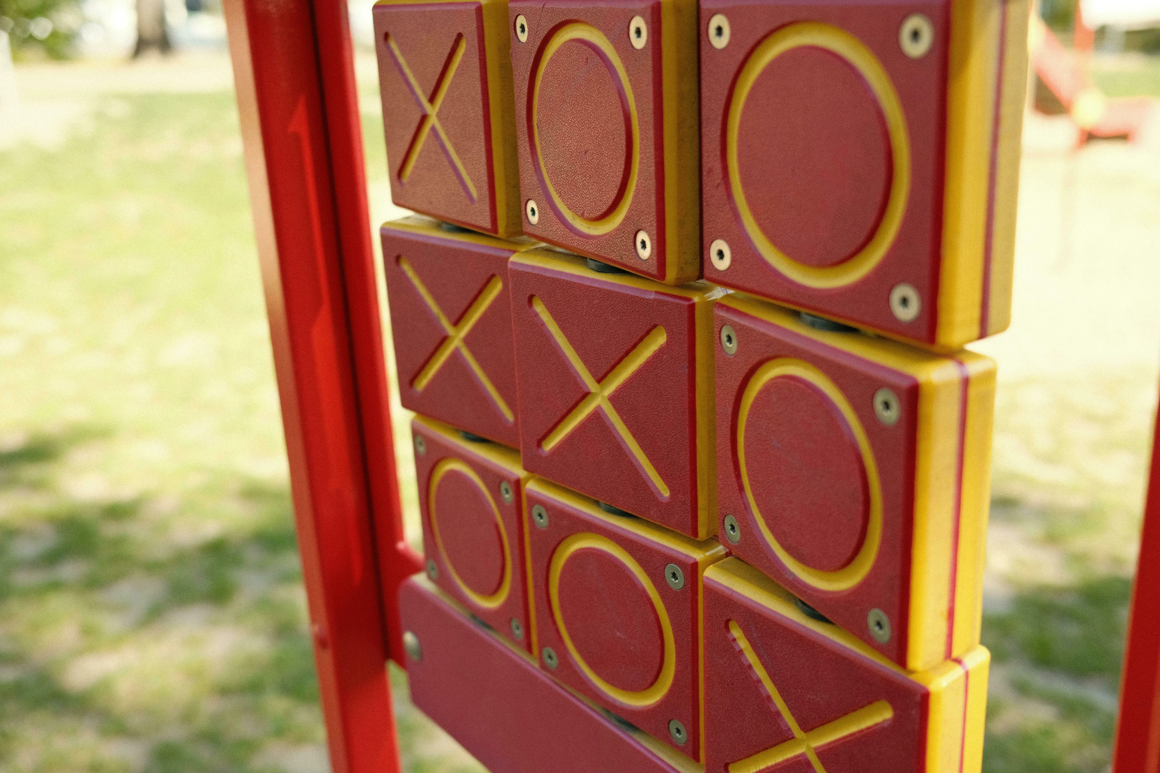 A close-up of a red and yellow noughts and crosses game on a playground, perfect for an English words quiz.