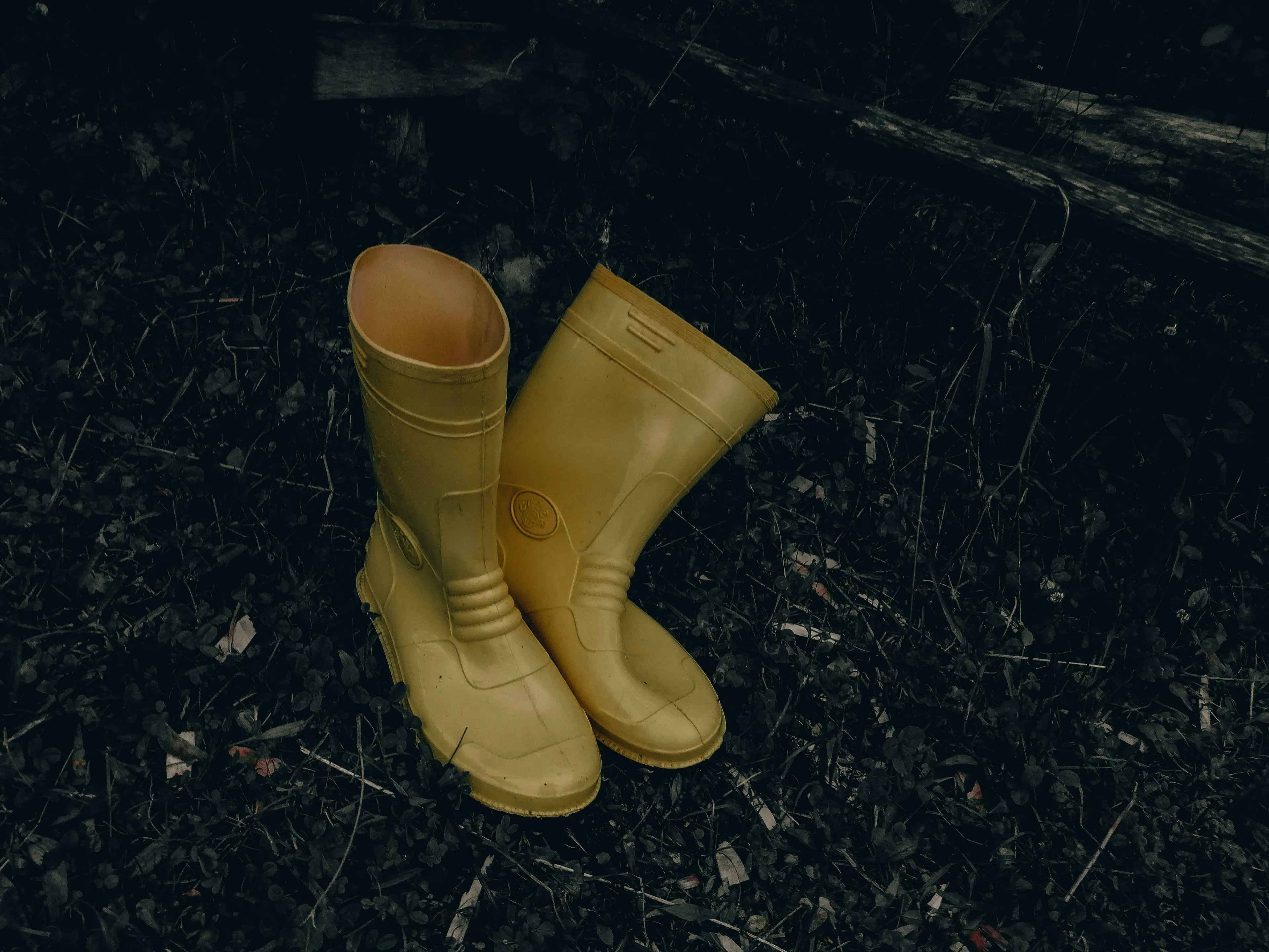 A pair of yellow rain boots, or rubber boots, on dark ground, highlighting differences in American vs British English words.