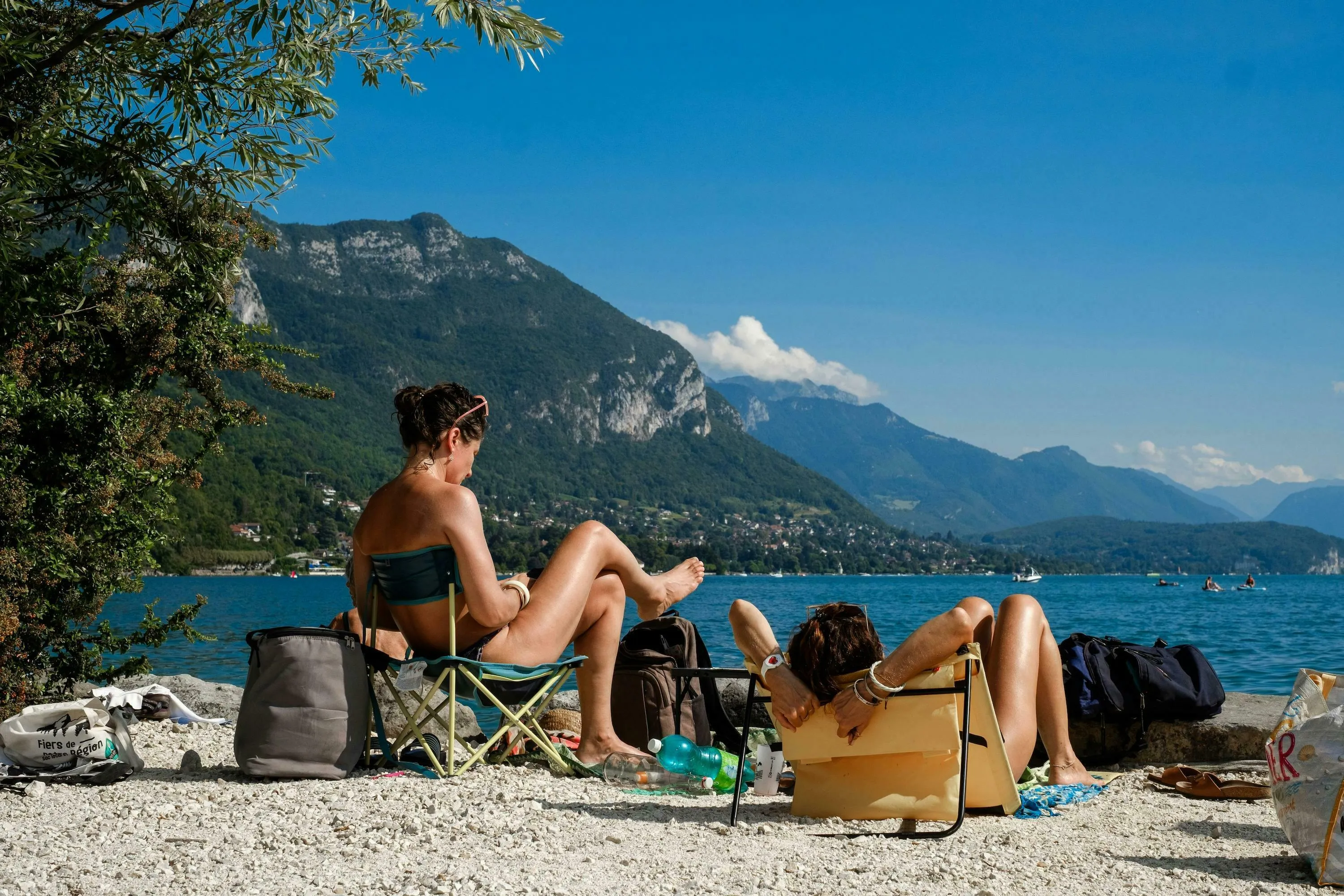 Two people relax by a lake with mountains in the background, enjoying a British English Words quiz during their holiday.
