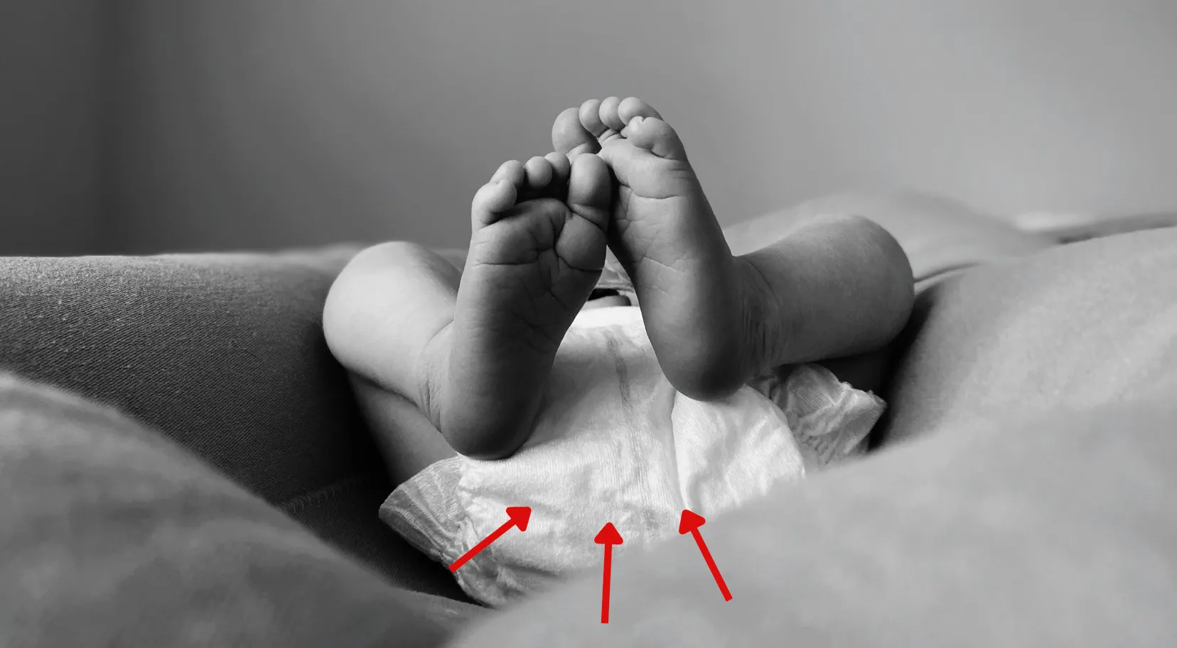 Black and white close-up of a baby's feet and diaper, with red arrows pointing at the diaper, useful for an American vs British English words quiz.