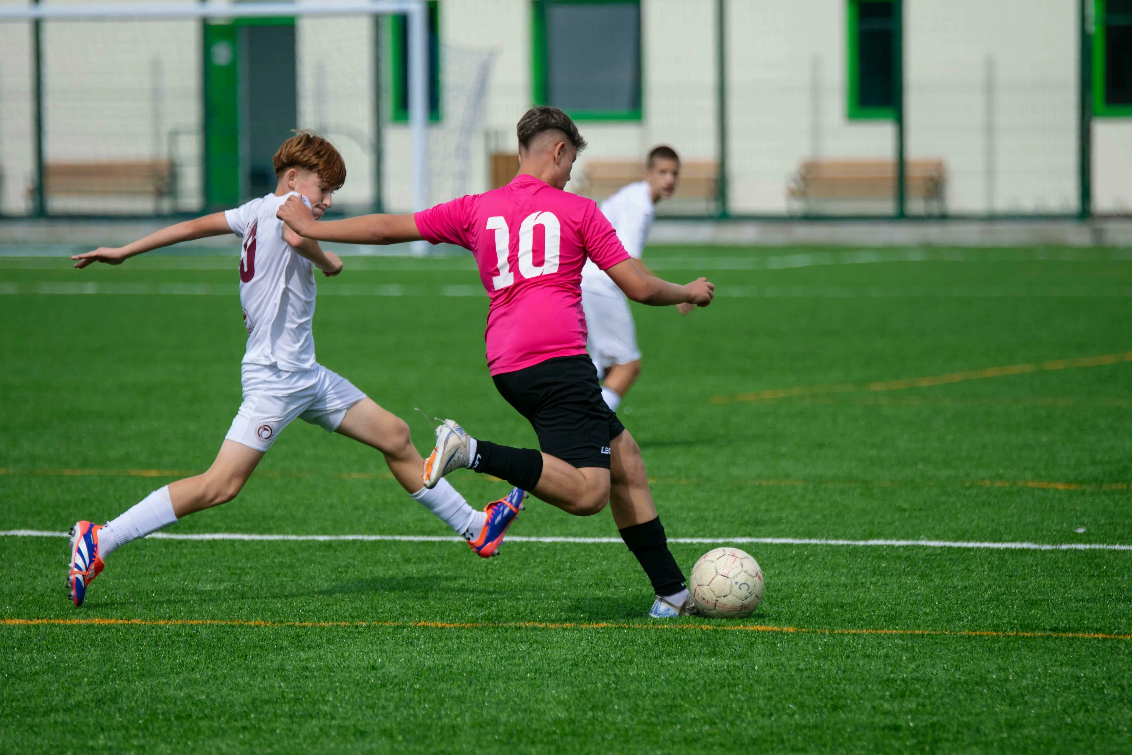 Two young men playing American vs British English words quiz sport, running on a green field with a soccer ball.