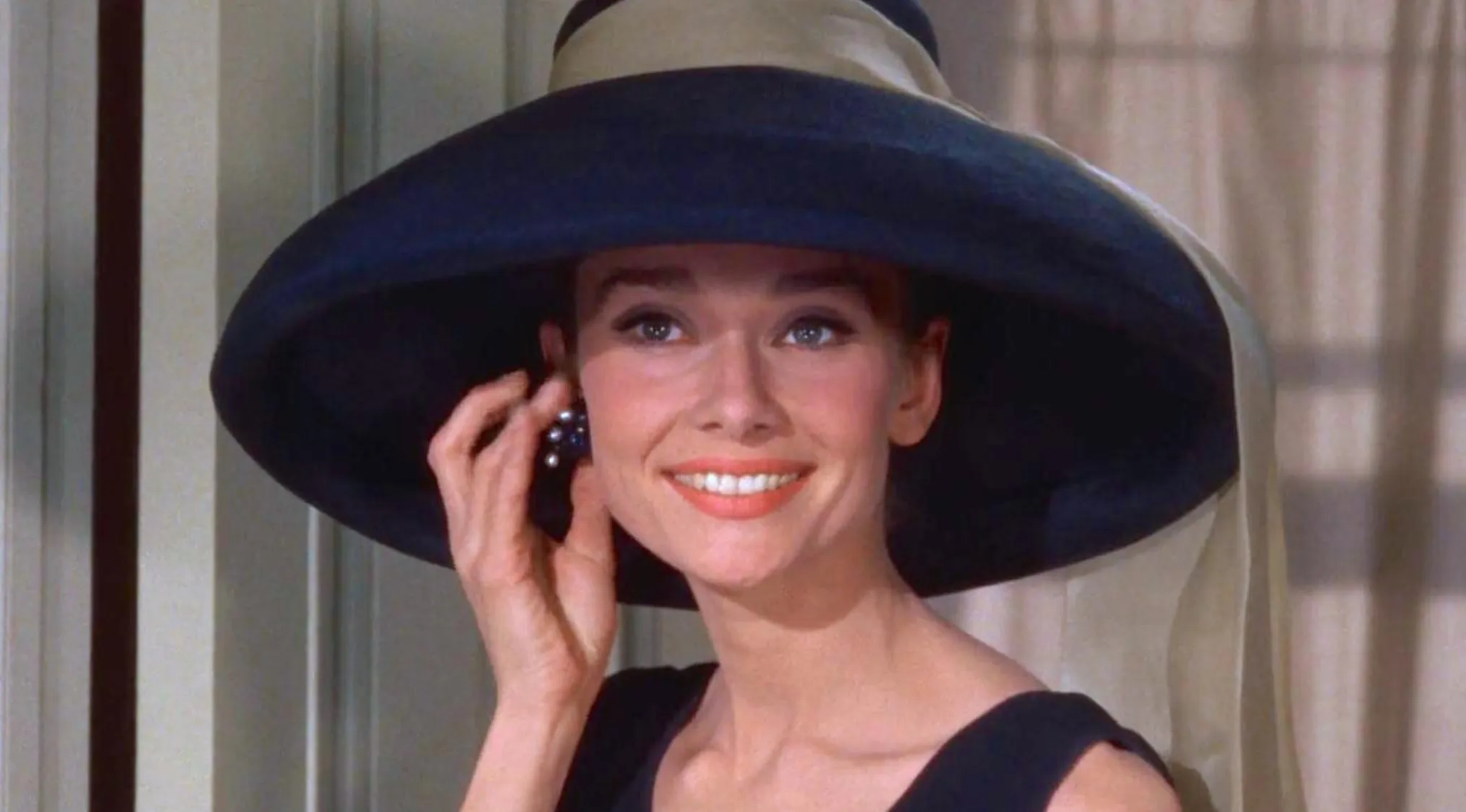 A famous person, a British actress, smiling and wearing a wide-brimmed hat, touching an earring.