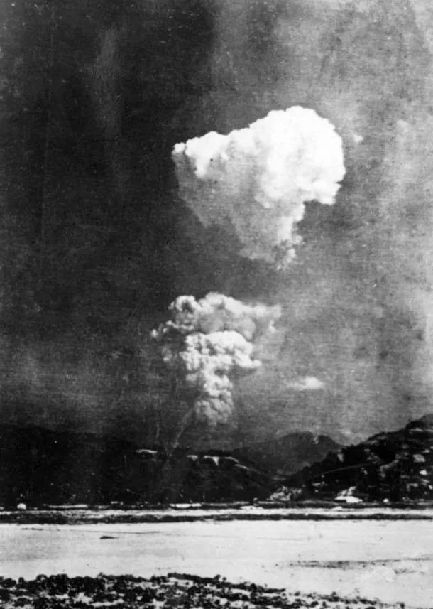 Black and white photo shows two large mushroom clouds, signifying an atomic weapon explosion, over a city in 1945. History question.
