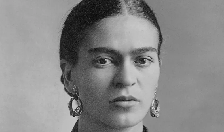 Black and white portrait of Frida Kahlo with dark hair, a subtle unibrow, and large earrings. School Questions.