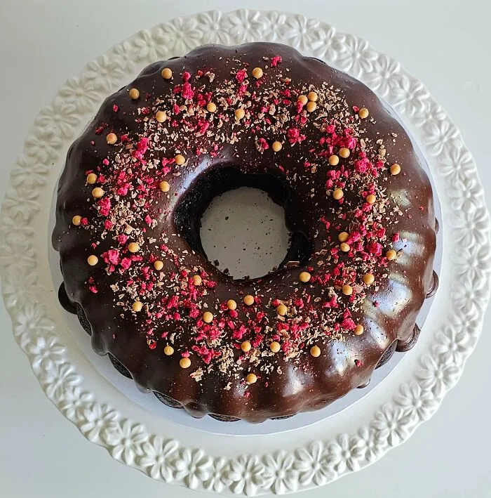 Chocolate bundt cake with glossy glaze and sprinkled toppings on white plate