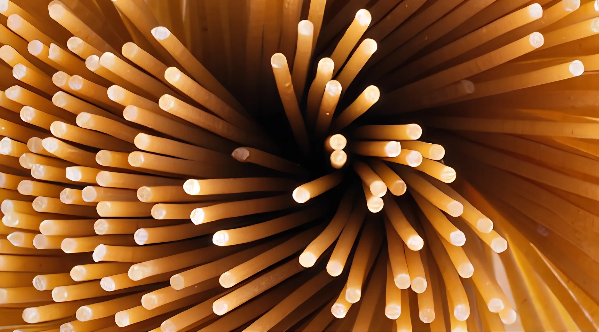 A zoomed-in image of dry spaghetti strands with glowing ends, fanning out from a dark center.
