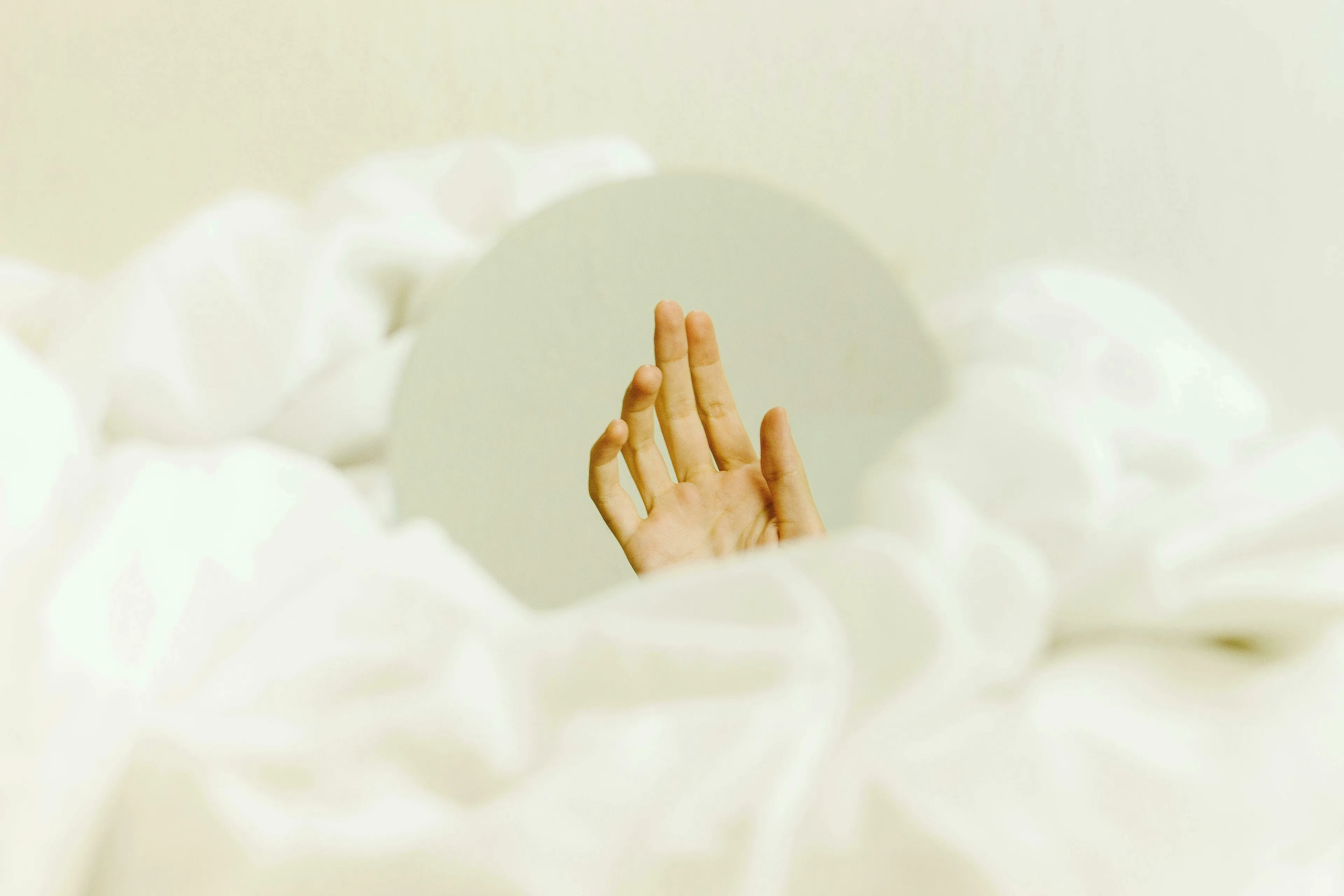 A pale hand reaches upwards from a bed of white, fluffy material into a soft, light background, evoking the General Knowledge Big Ideas Quiz.