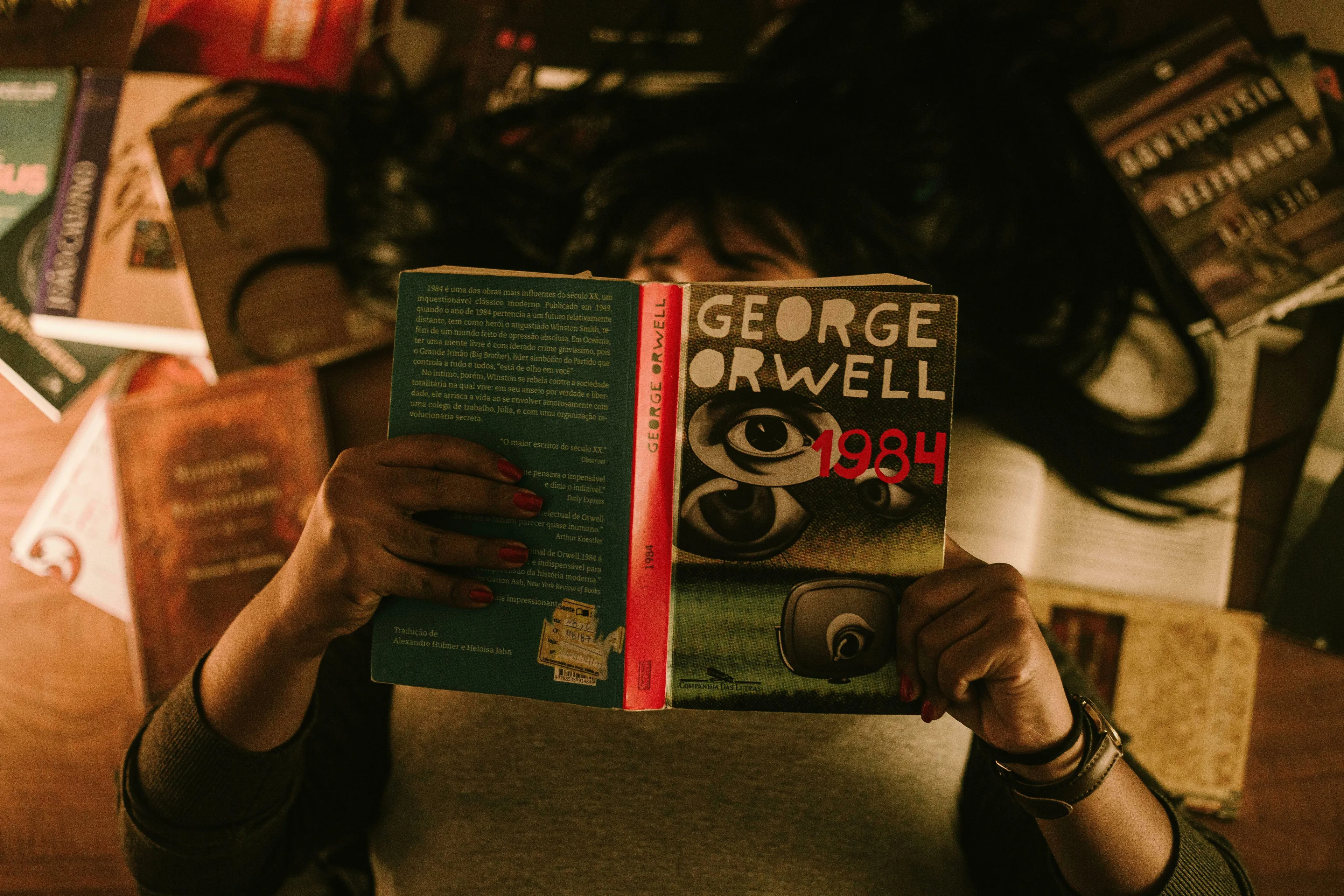 A person holding George Orwell's 1984 book, surrounded by other books. A general knowledge quiz Big Ideas concept.