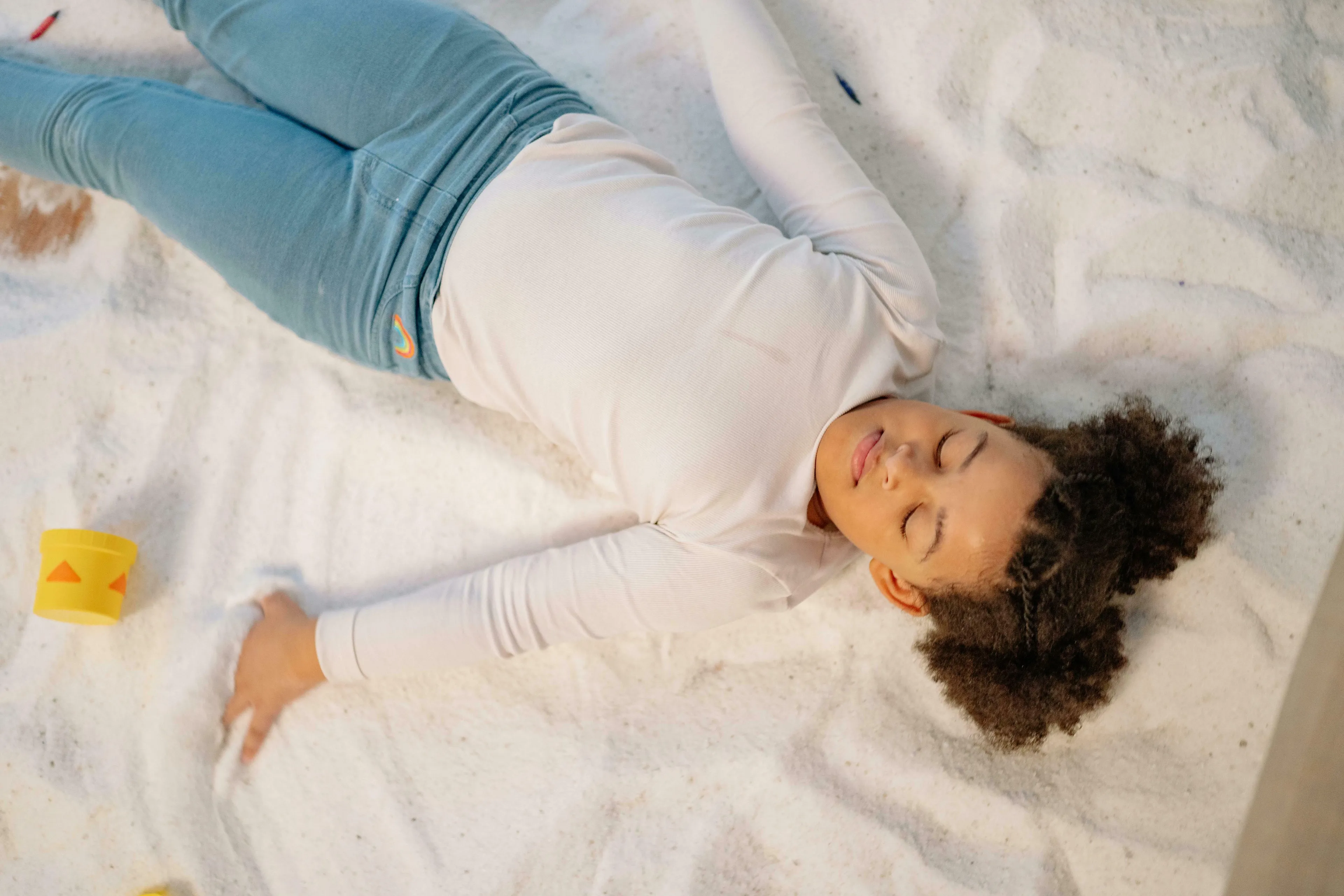 A child with curly hair and light blue jeans resting on a white blanket. General knowledge big ideas.