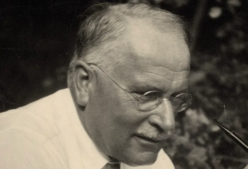 Carl Jung, a thinker in psychology, wearing glasses and a shirt, looking down, possibly smoking a pipe.