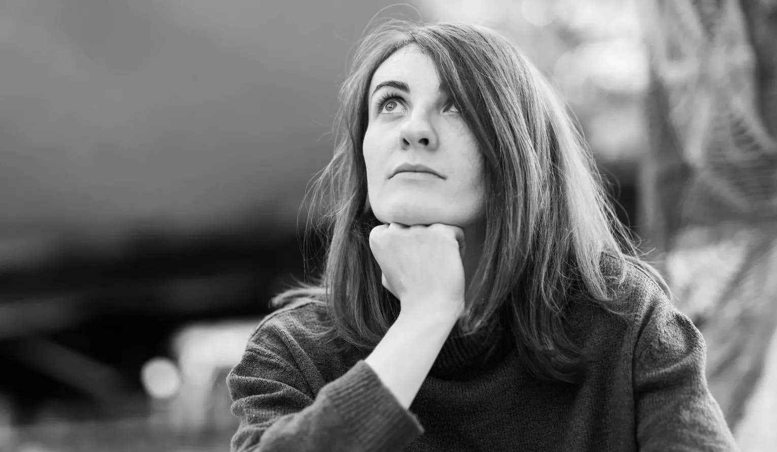 Black and white image of a thoughtful woman looking up, resting her chin on her fist. General knowledge and ethics.