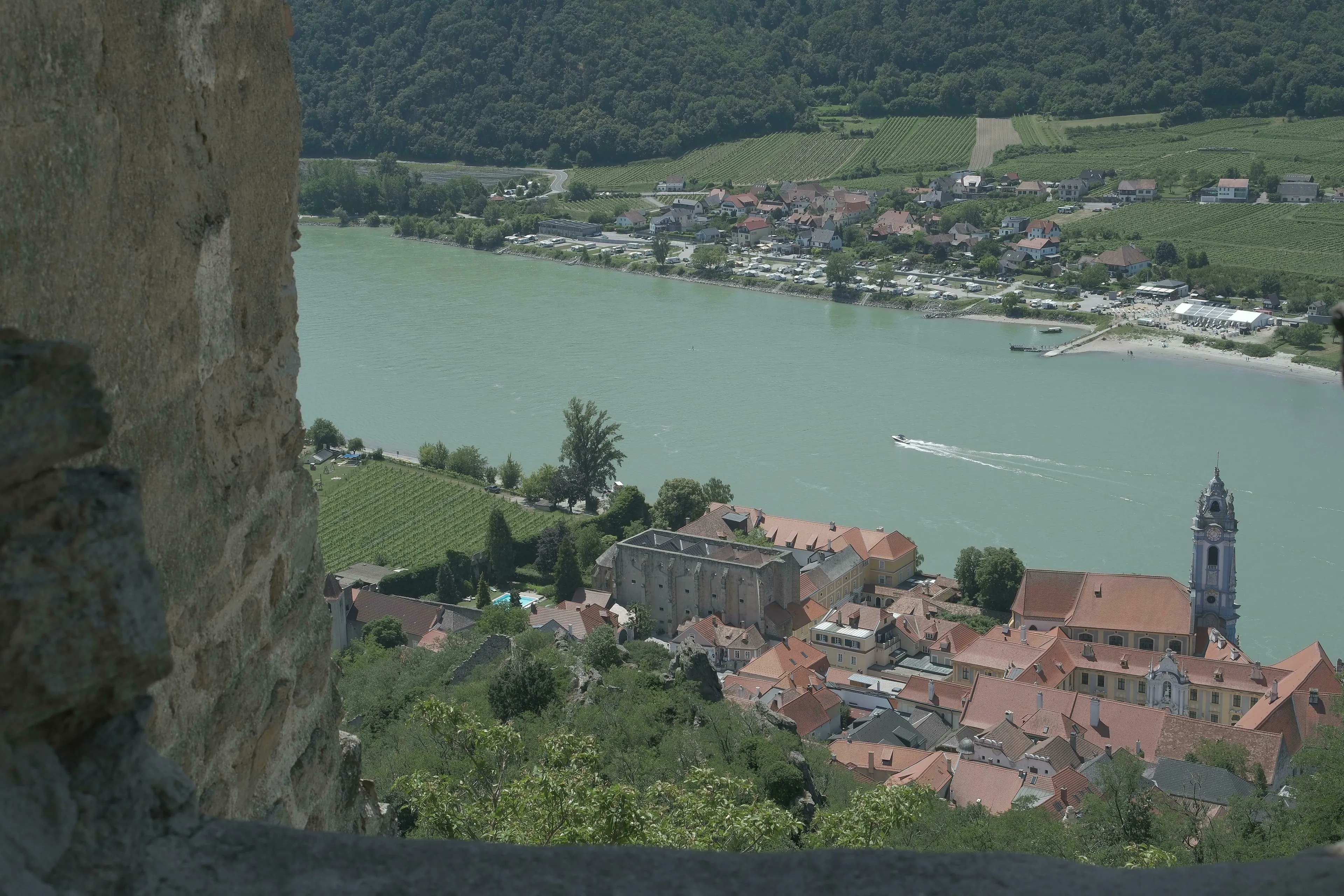 A high-angle view of a European river town with red-roofed buildings and a boat on the water, answering a General Knowledge question.