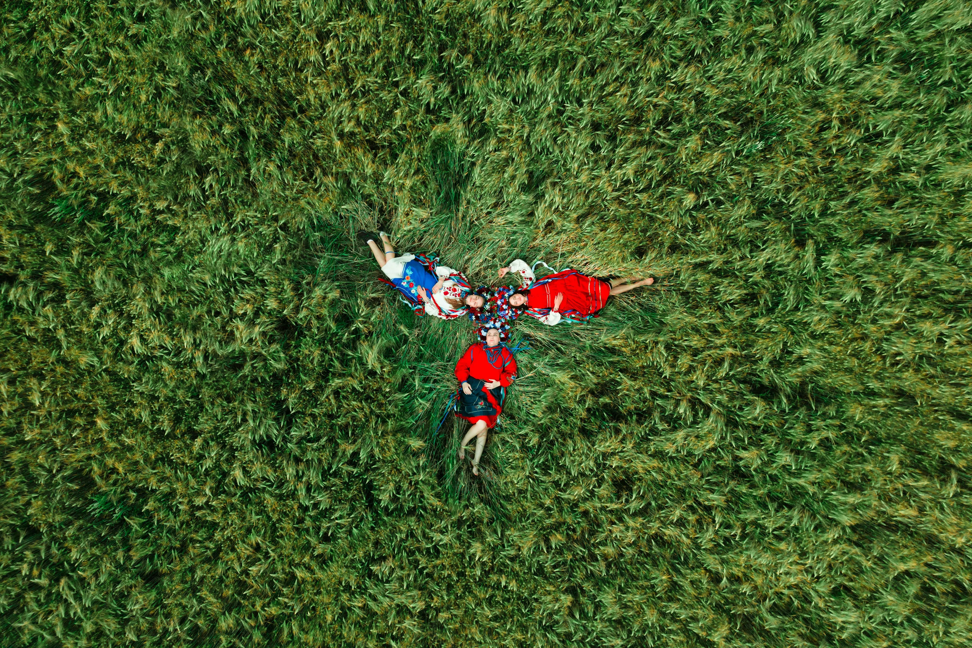 Aerial view of four women in traditional clothing lying in green grass, forming a star shape, related to General Knowledge.