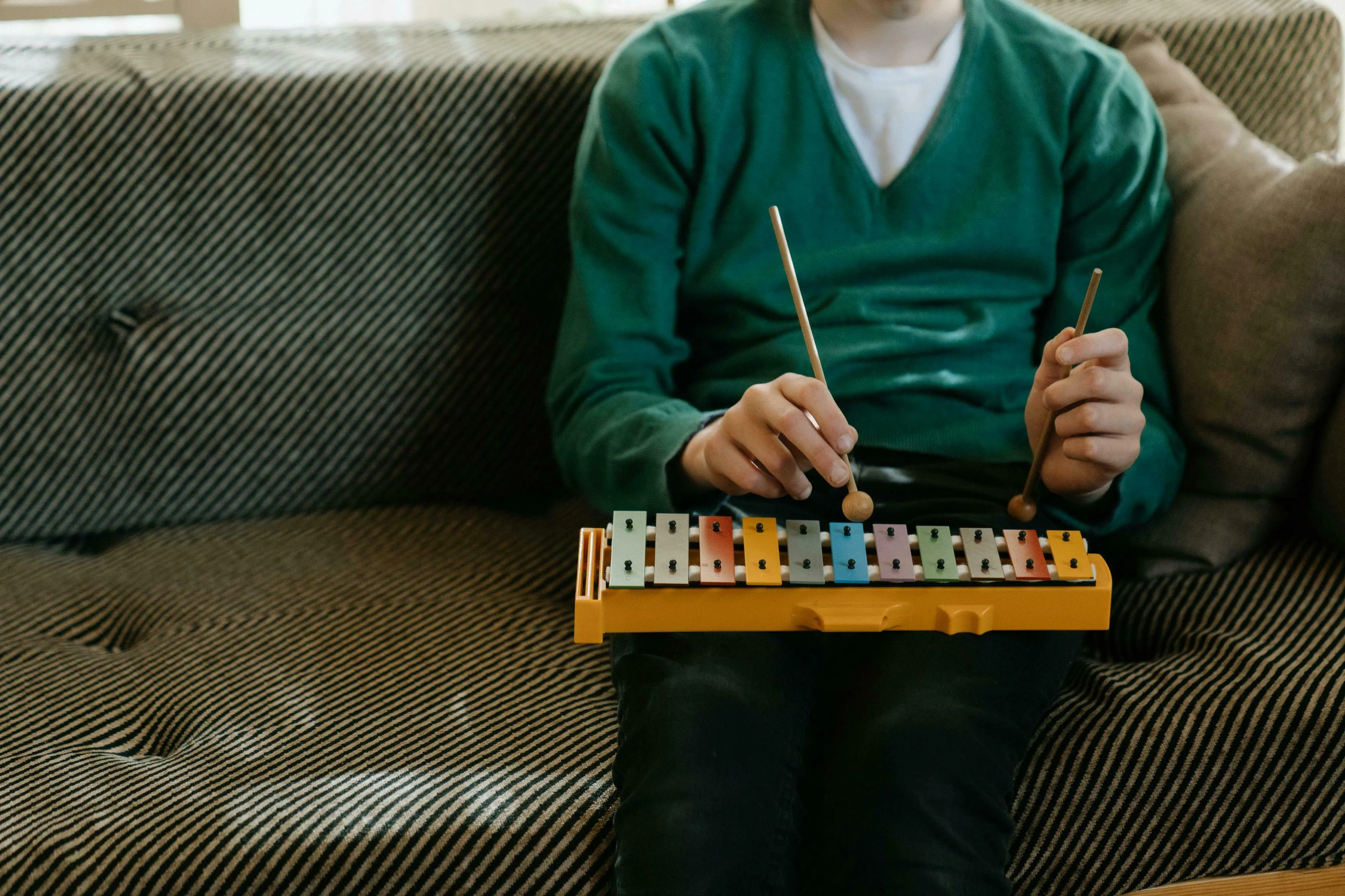 A person in a green sweater playing a colorful musical percussion instrument on a striped couch, for General Knowledge.