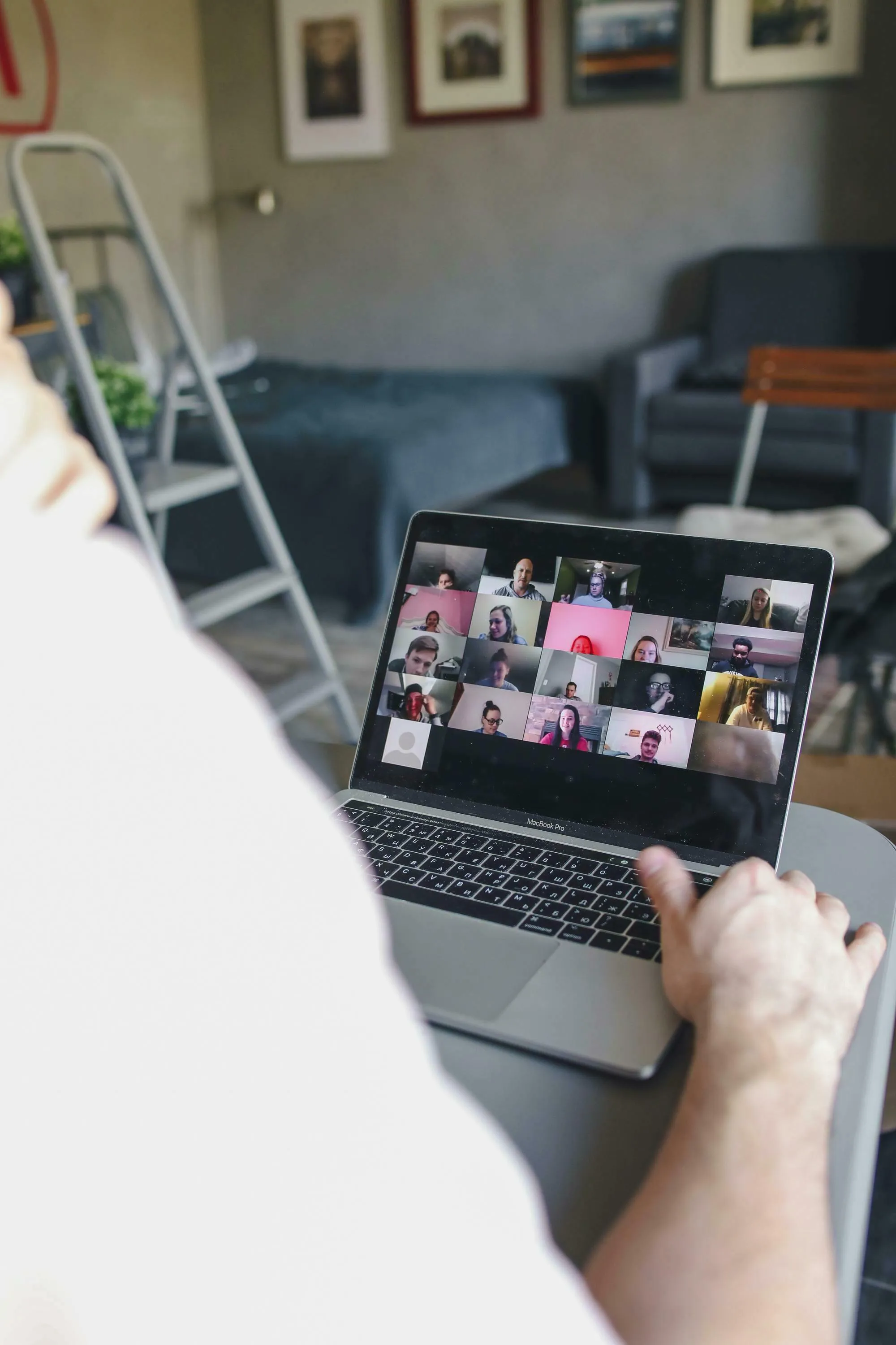 Over-the-shoulder view of a person on a laptop displaying a Zoom video communication meeting during remote work. General knowledge.