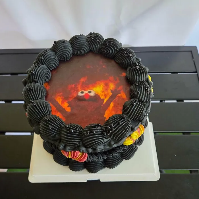 Round cake with black frosting and an image of fiery Elmo character on top