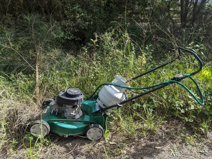 A green lawnmower with a propane tank attached, sitting in tall grass. A clever solution for powering the machine.