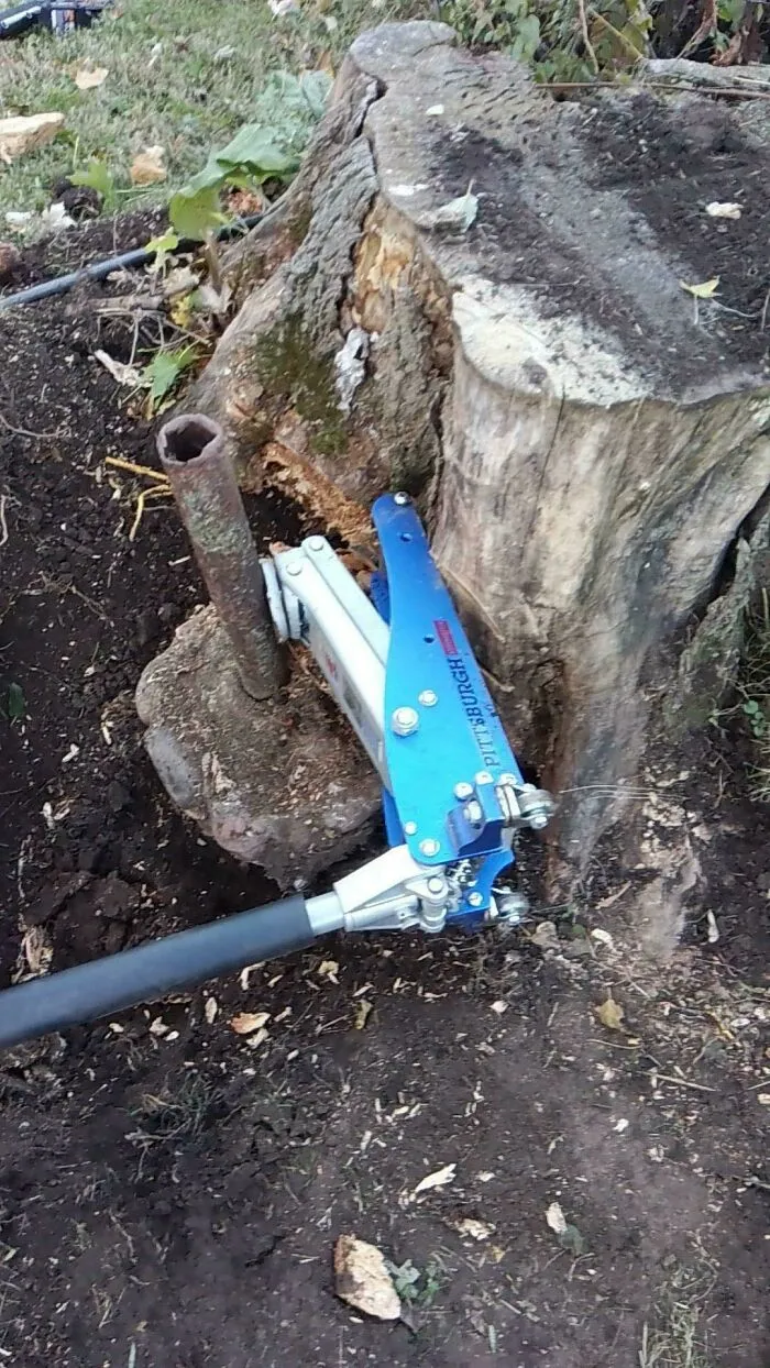 A tree stump being pulled out of the ground using a blue jack and a metal pole. A clever solution for stubborn junk.