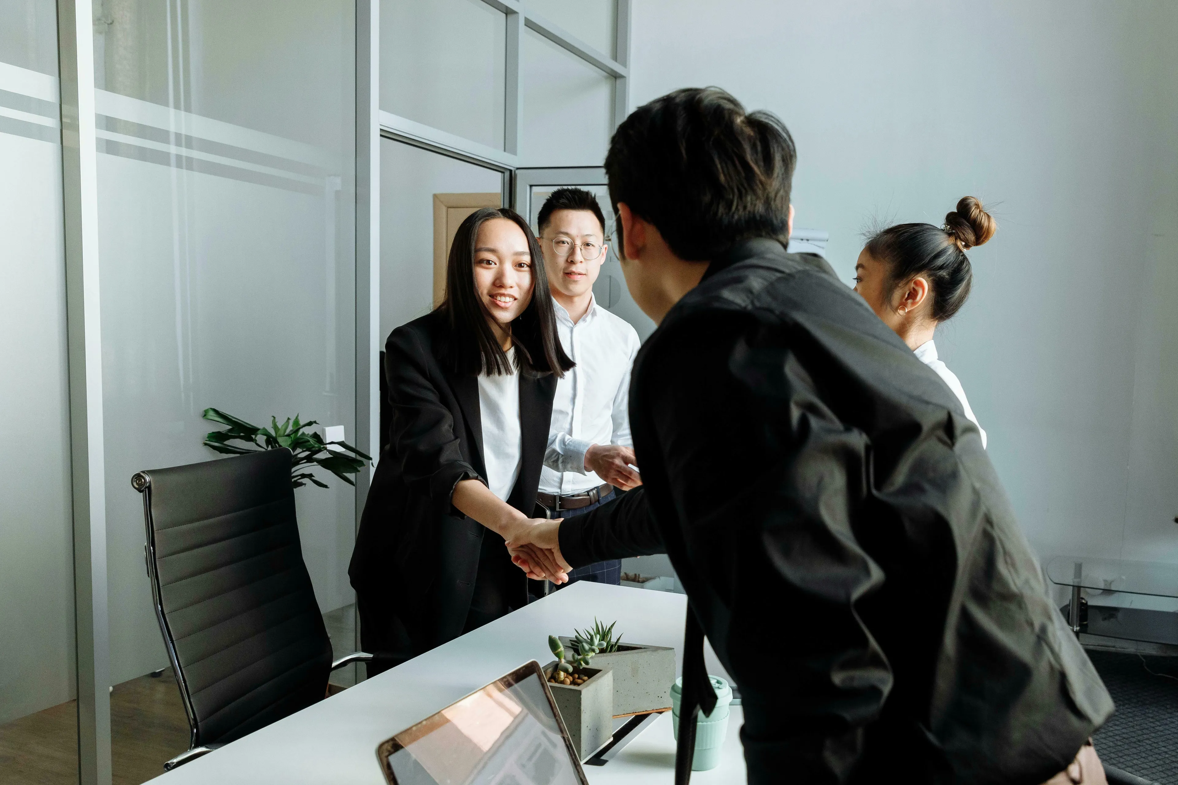 Two colleagues shake hands, introducing a new team member. They embrace the change of a new team at work.