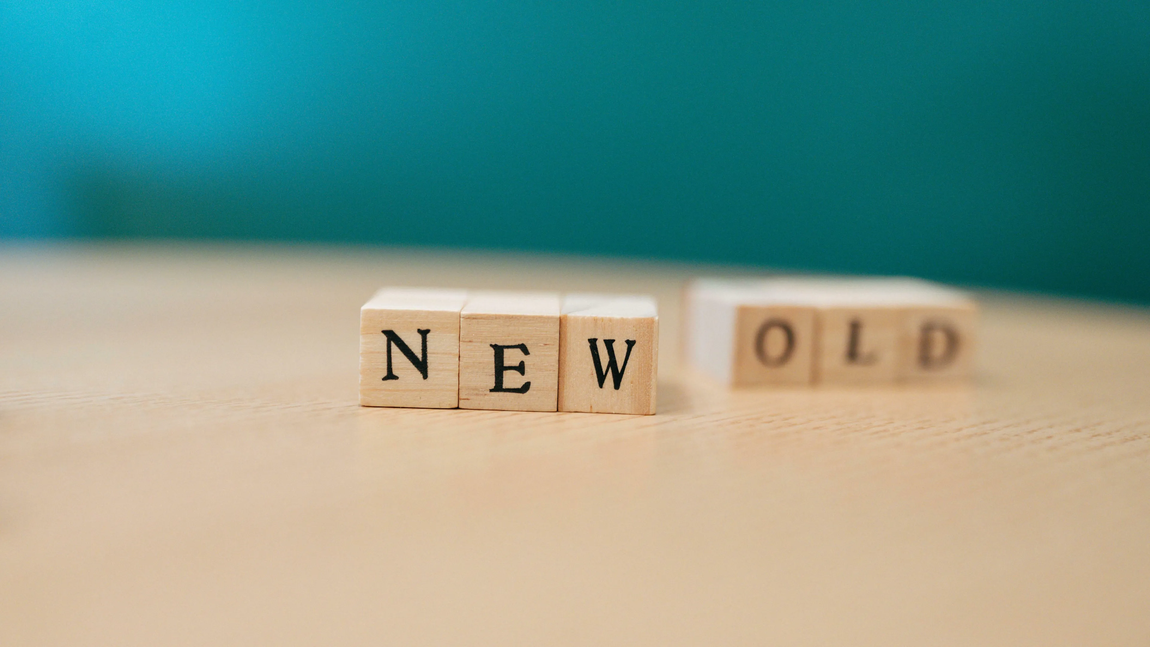 Wooden blocks spell NEW in focus, with blurry OLD behind them, symbolizing change and reinvention.