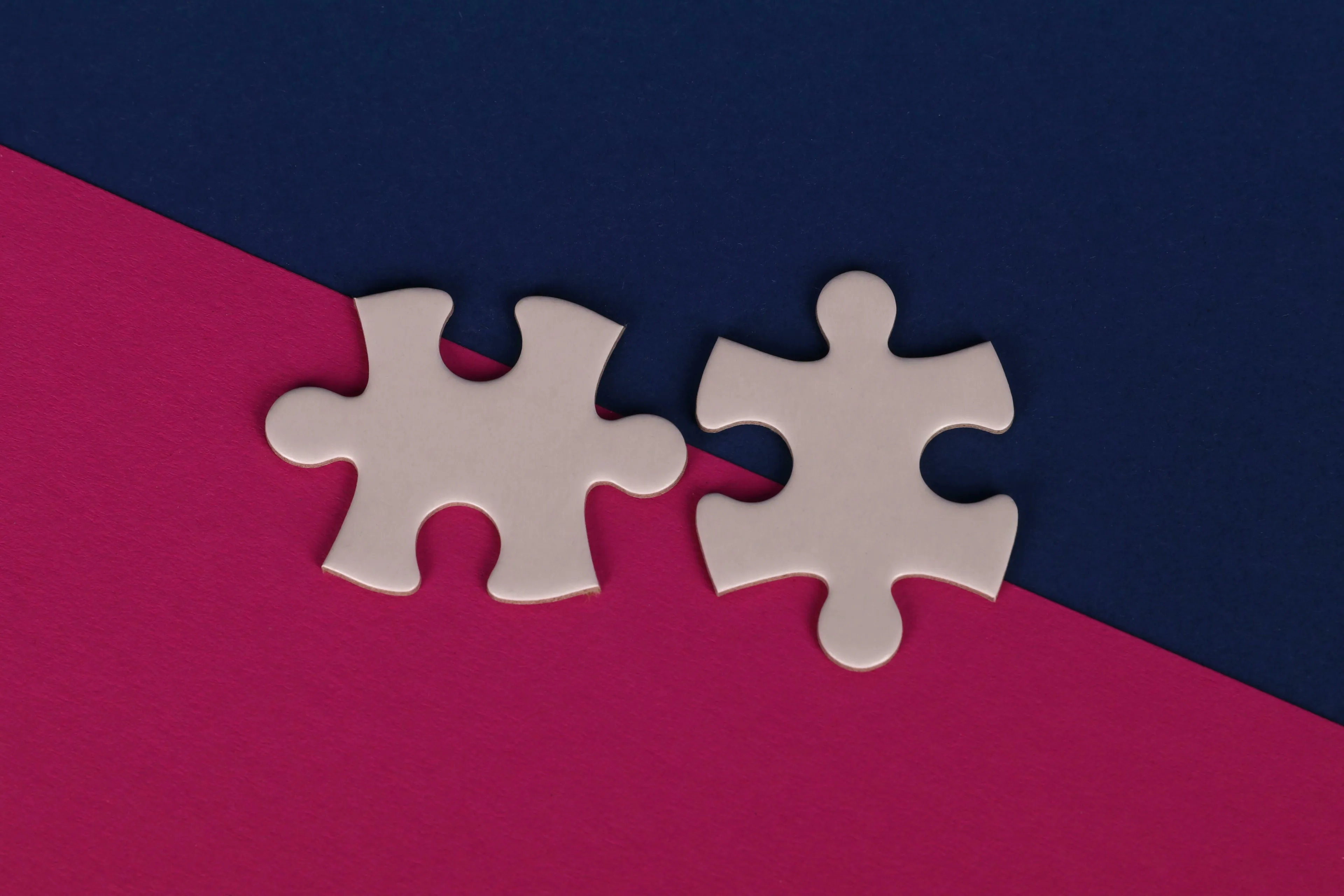 Two white puzzle pieces on a split background of dark blue and magenta, symbolizing connection or finding meaning in change.