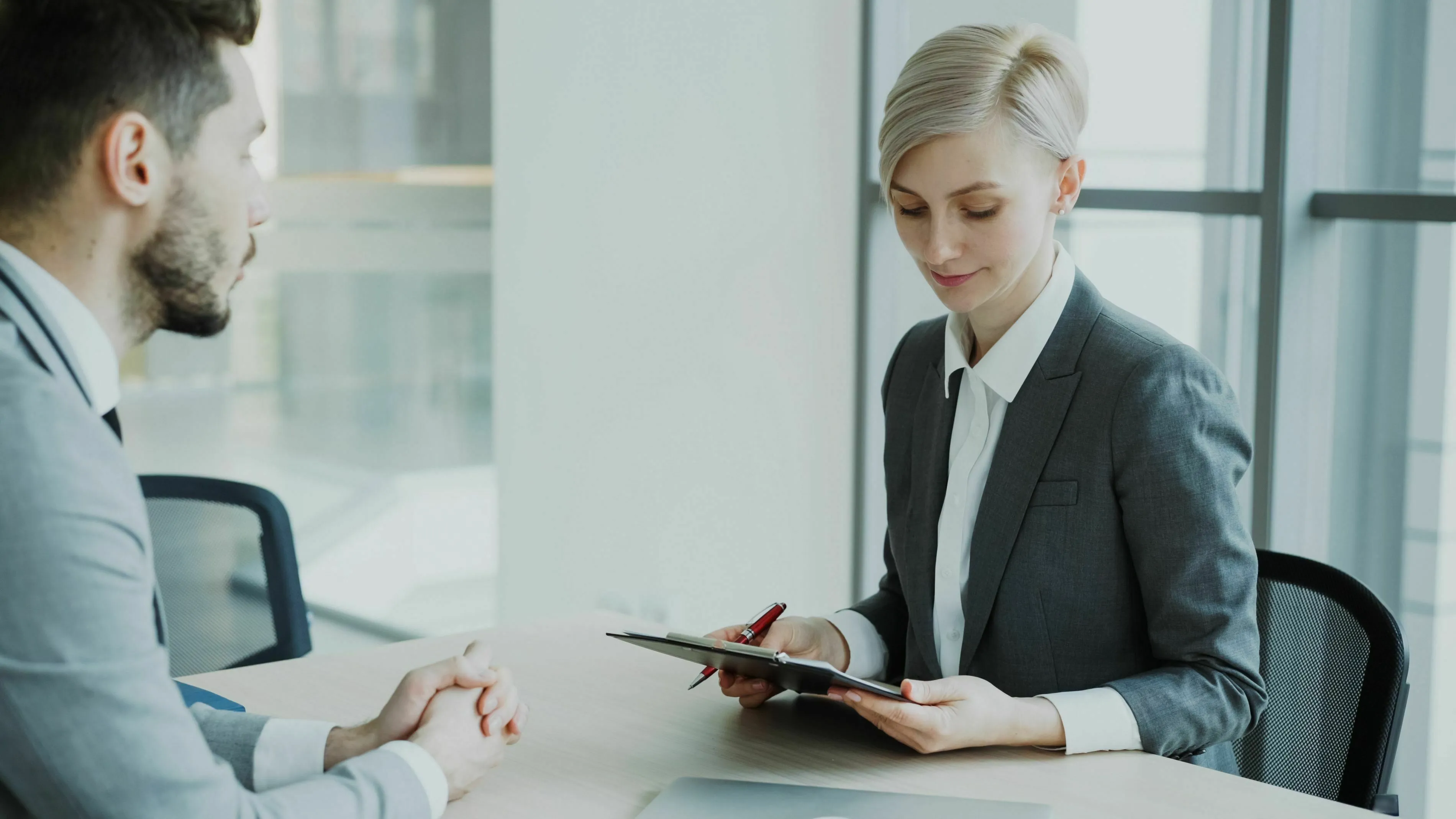 Two professionals discussing a job role change. Woman holds a clipboard while man listens, demonstrating how to react to change.