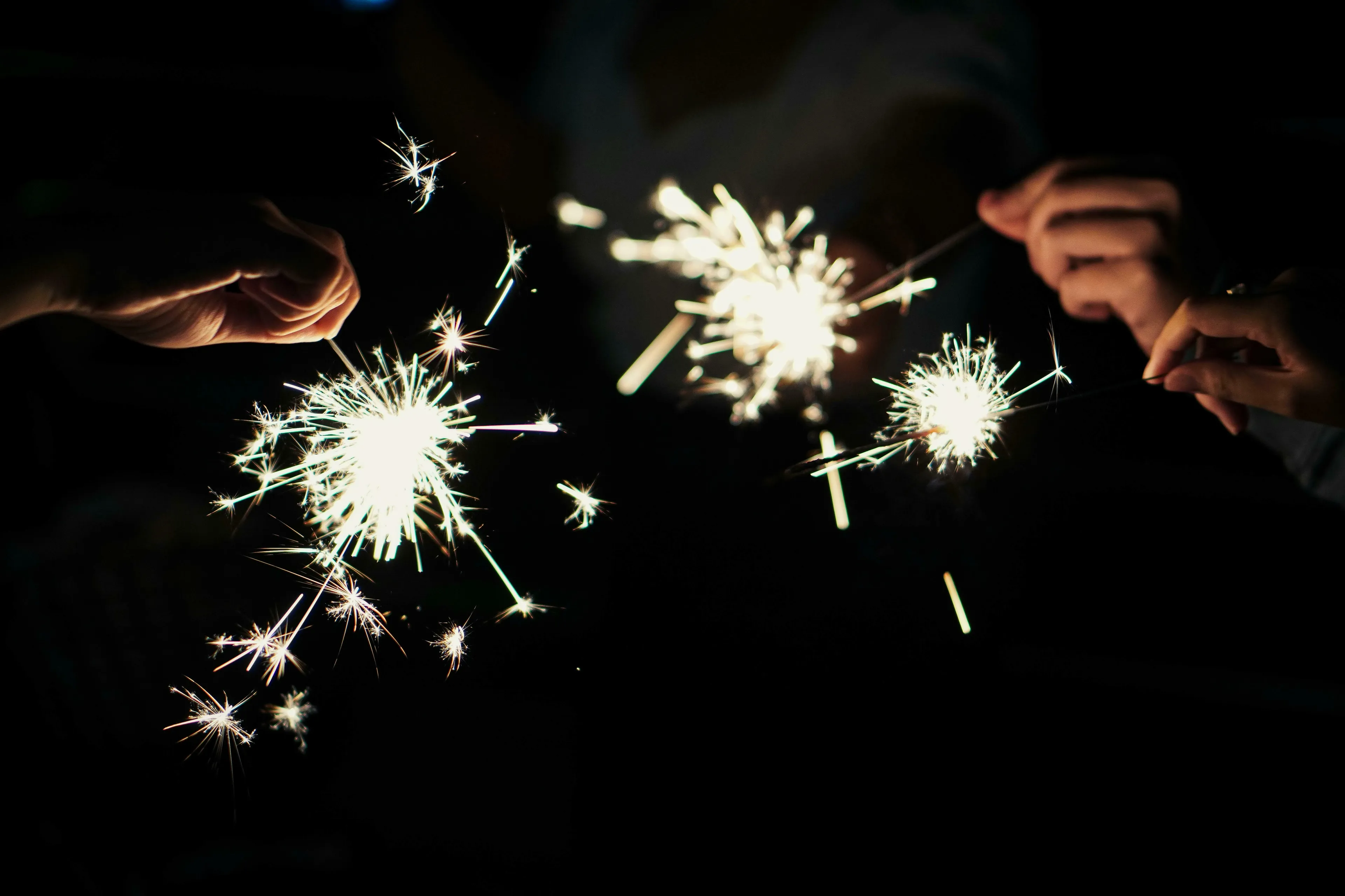 Multiple hands hold brightly burning sparklers in the dark, symbolizing the new year and the general stance on the year ahead.