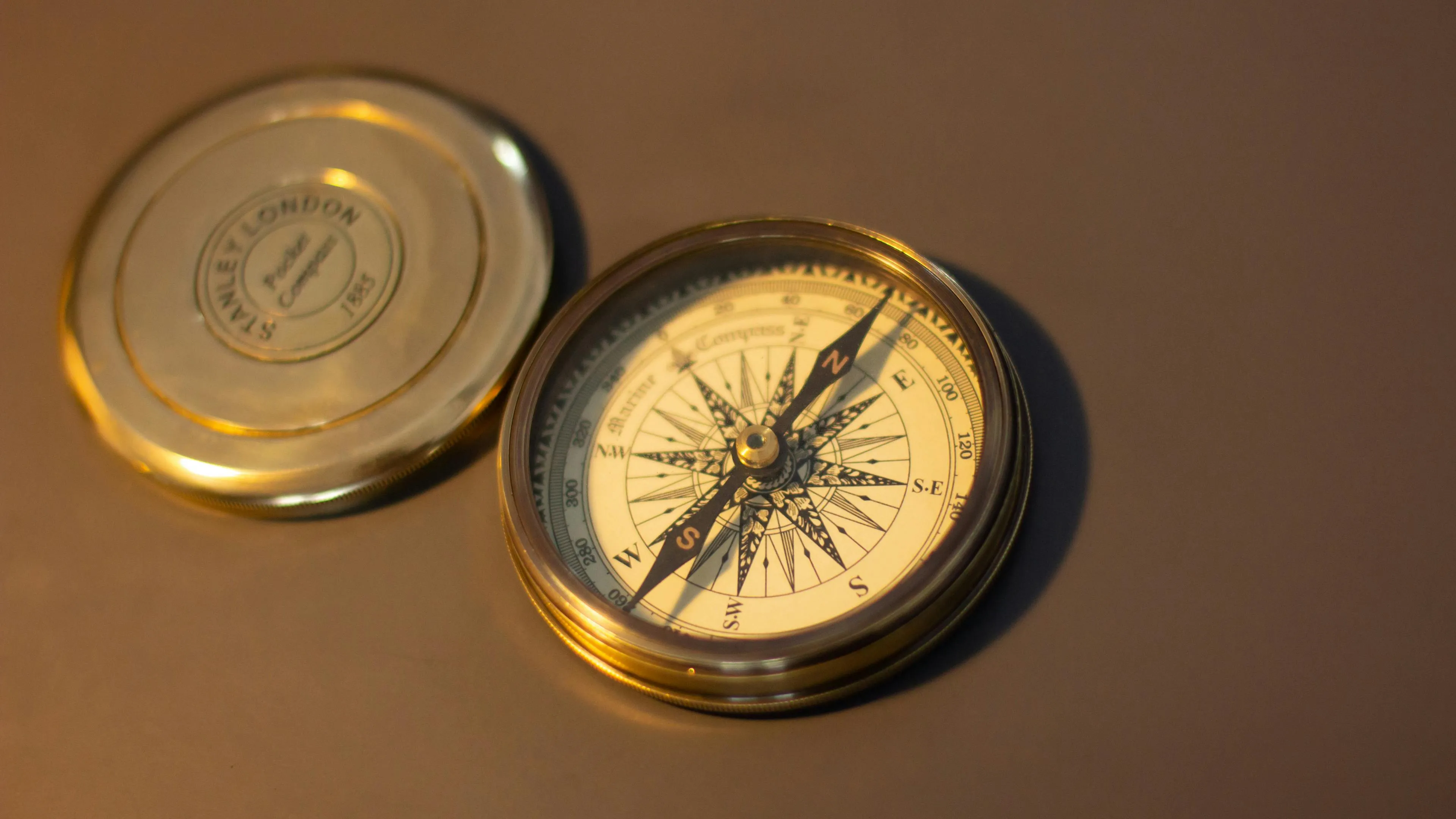 A close-up of a vintage brass compass with its lid open, displaying the detailed face and needle, on a dark surface.