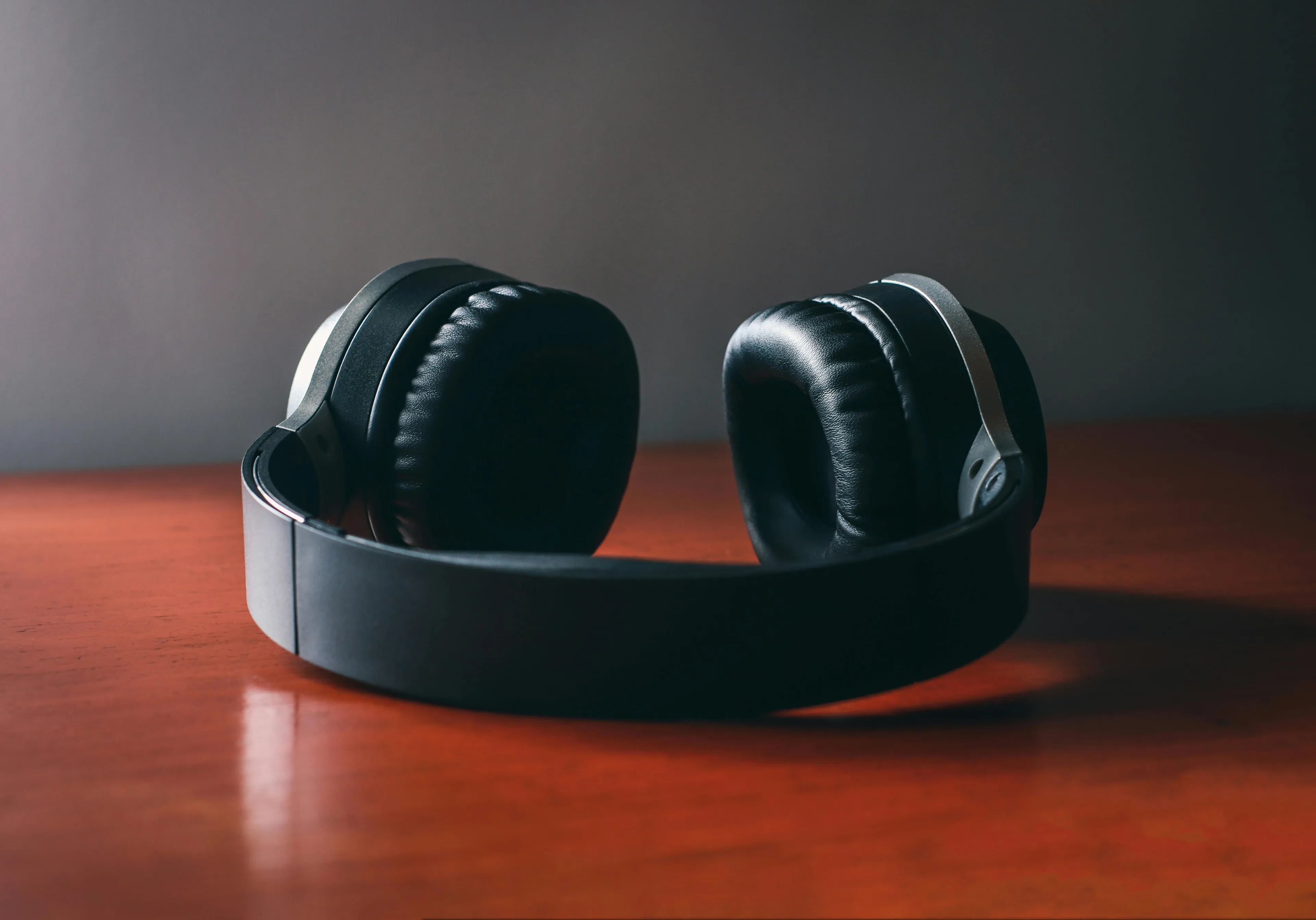 A pair of black wireless headphones resting on a warm, wooden surface with a grey background.