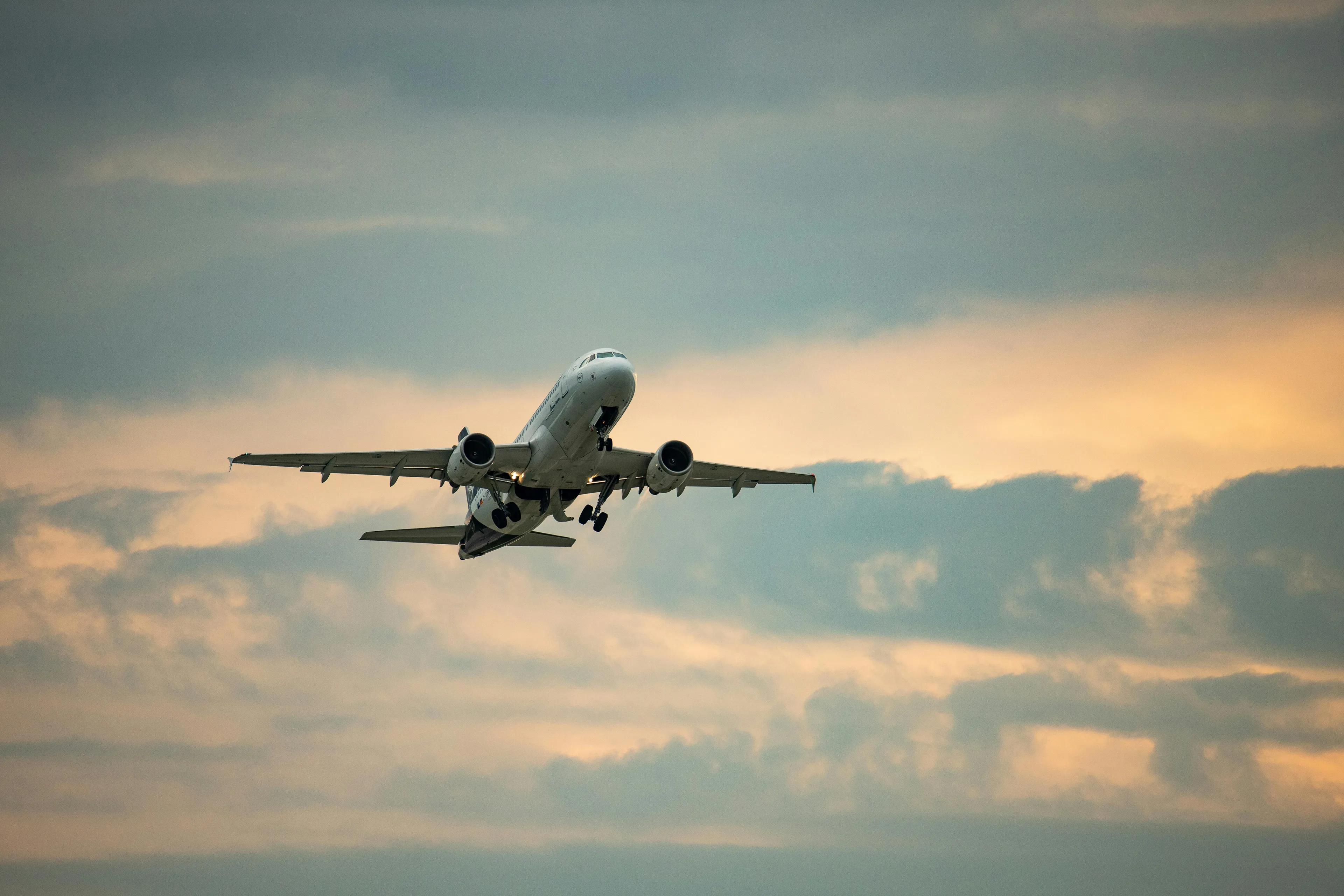 A white commercial airplane takes off against a cloudy sky with warm sunset hues. An invention, the airplane, soars.