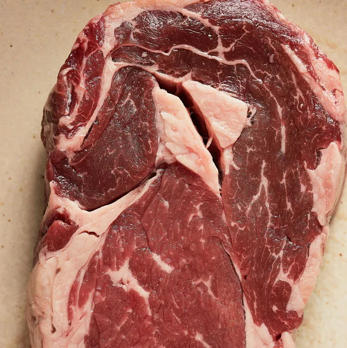 A close-up of a raw ribeye steak, showcasing the marbled red meat and white fat. One of the weirdest packages.