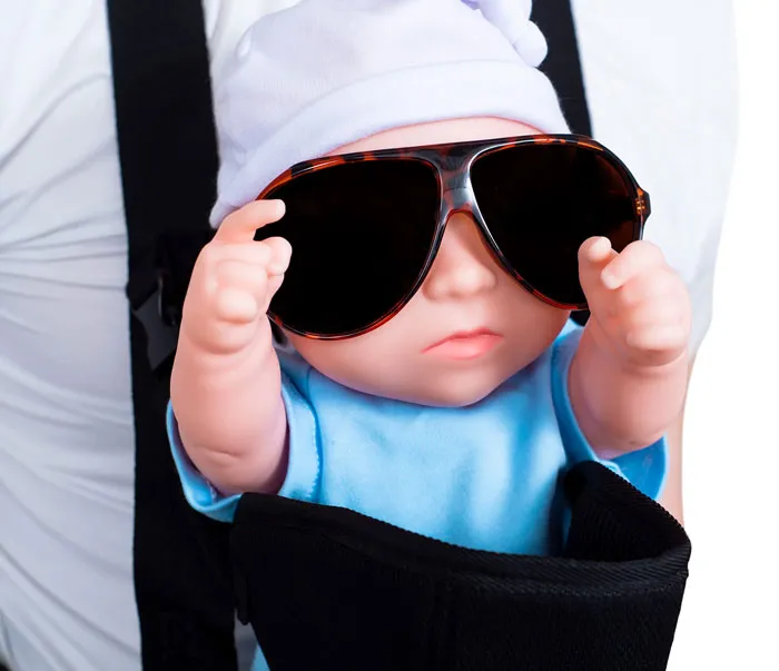A baby doll in a carrier wears a white hat and large sunglasses, looking cool. Perhaps one of the weirdest packages.
