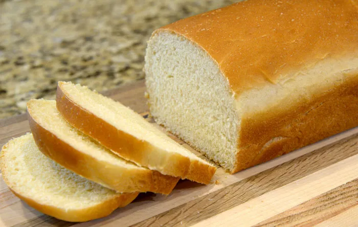 A loaf of white bread, partially sliced, on a wooden cutting board, looking like one of the weirdest packages.