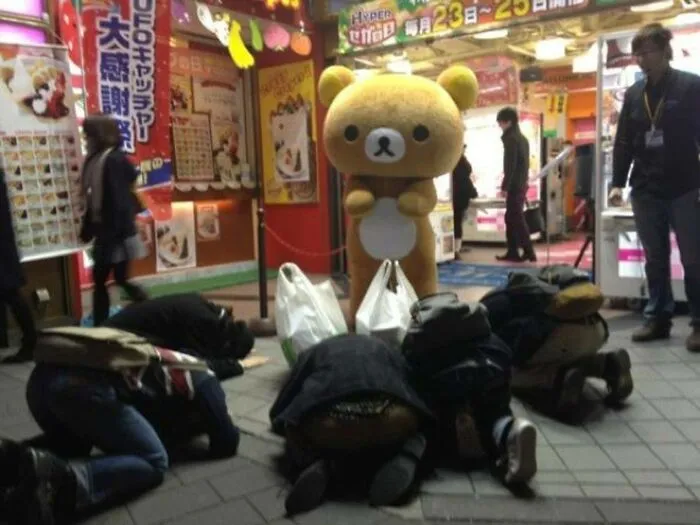 People bowing down in front of giant cute bear costume figure