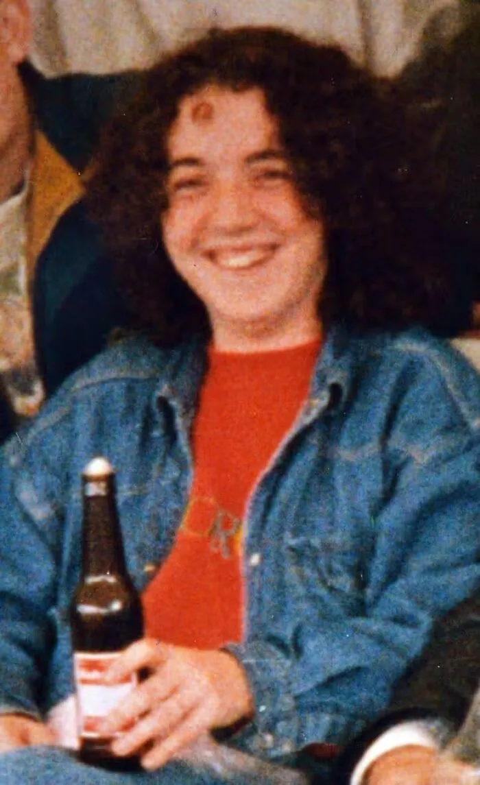 A young person with curly hair, smiling and holding a beer bottle. This image evokes disturbing death stories.