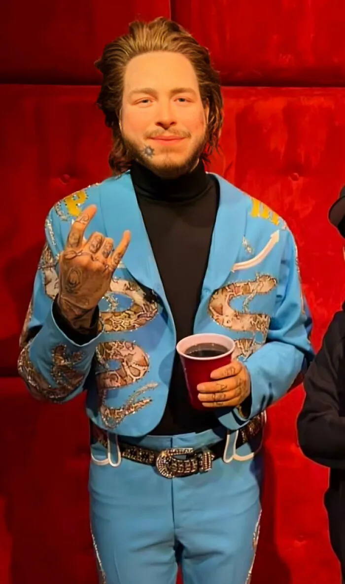 Celebrity wax figure wearing a blue decorated outfit holding a cup and making a hand gesture