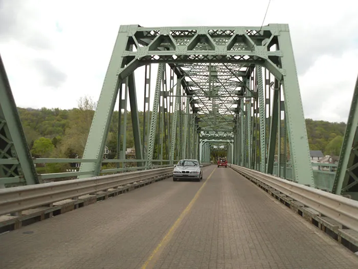 A sturdy green metal truss bridge with two cars driving on it, one silver and one red, representing US States.