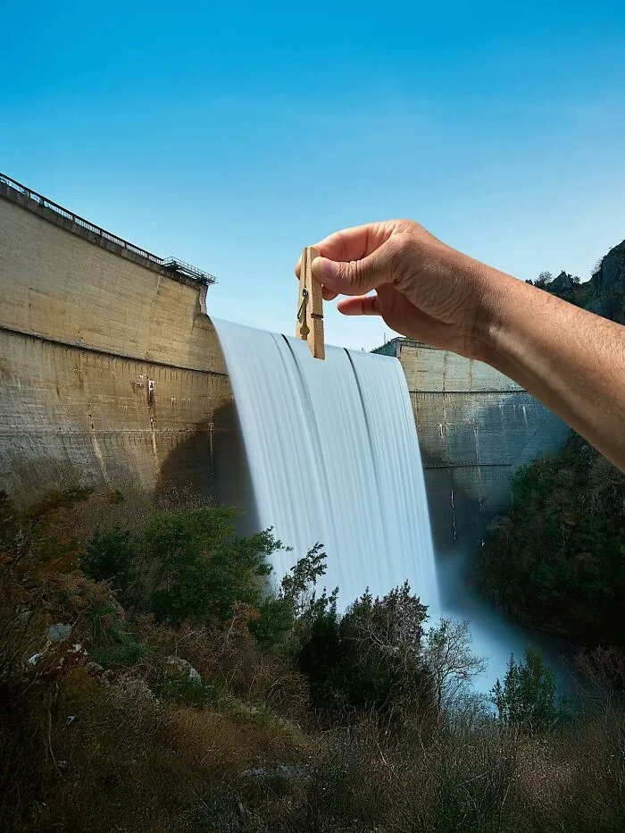 A hand holding a clothespin, making it appear to hold back a dam with a waterfall. This photo manipulation makes simple objects look like parts of cities.