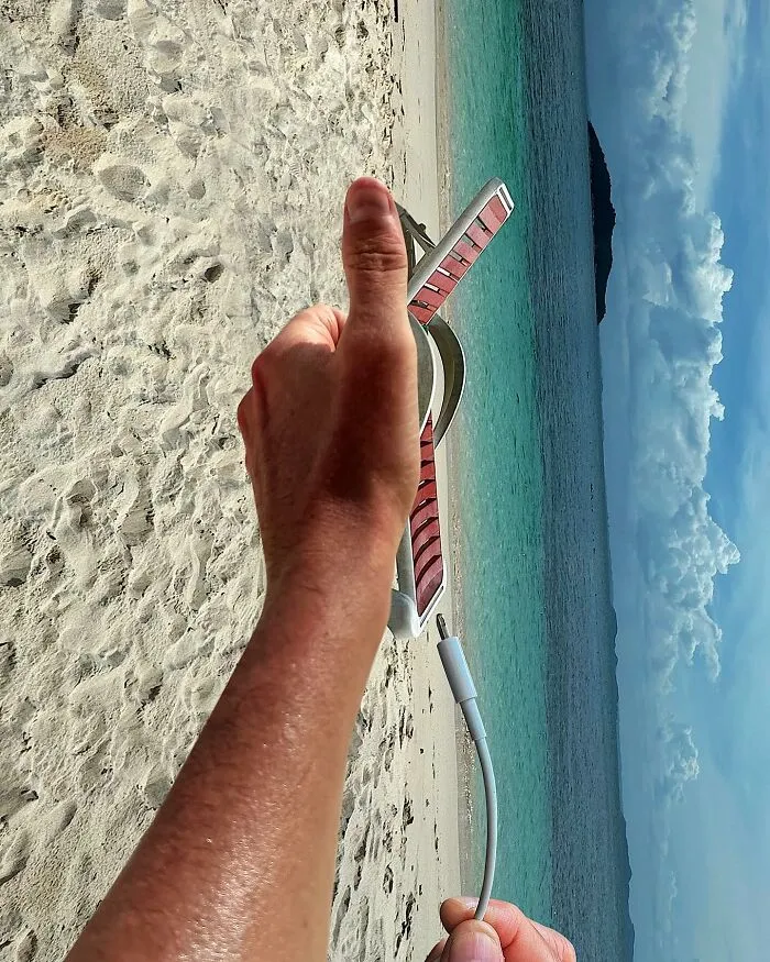 A hand holding a USB cable and a device on a beach, part of a clever photo manipulation making simple objects look like parts of cities.