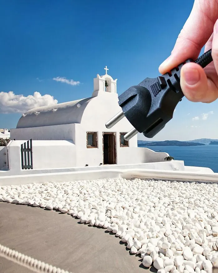 A hand holding an electrical plug towards a white church building, a clever photo manipulation making simple objects look like parts of cities.