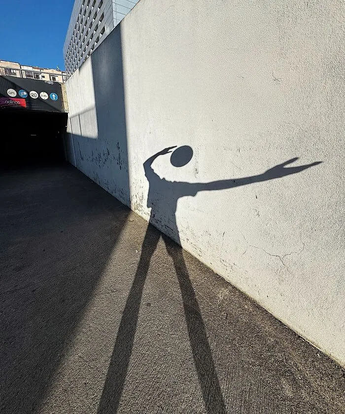 A long shadow of a person on a white wall, holding a small object, creating a clever photo manipulation effect.